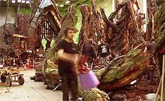 a man standing next to a pile of trees in a room filled with lots of junk