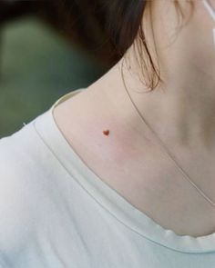 a woman with a small heart tattoo on her back shoulder and neck, wearing a white t - shirt