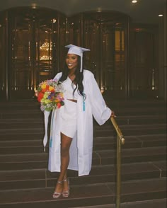 a woman wearing a graduation gown and holding a bouquet stands in front of some steps