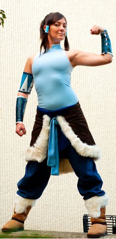 a woman in a blue top and brown pants is doing a kickbox pose with one arm raised