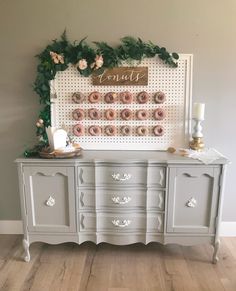 a white dresser with pink donuts on it and greenery around the top shelf