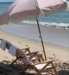 an umbrella and chair on the beach with towels draped over it's back,