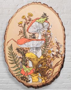 a wood slice with flowers and mushrooms on it in front of a white brick wall