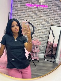 a woman taking a selfie in front of a mirror while wearing pink pants and a black shirt