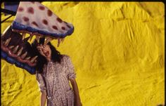 a woman holding a fake pizza on top of her head in front of a yellow backdrop