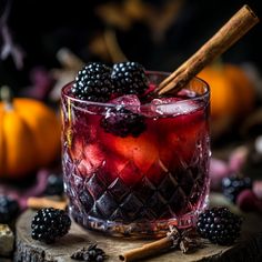 a glass filled with blackberries and cinnamon on top of a wooden table next to pumpkins