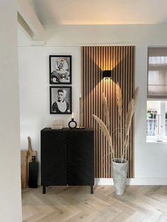 a vase with some plants in it next to a wooden paneled wall and pictures on the wall