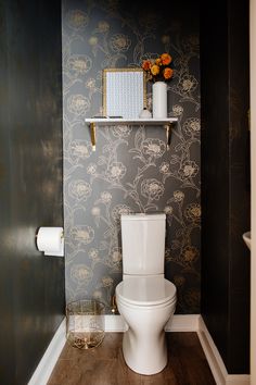 a white toilet sitting inside of a bathroom next to a wall papered with flowers