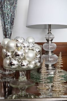 christmas decorations on a glass table with a white lamp and silver tree ornament