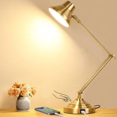 a desk lamp sitting on top of a wooden table next to a vase with flowers