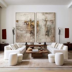 a living room with two large paintings on the wall and white couches in front of it