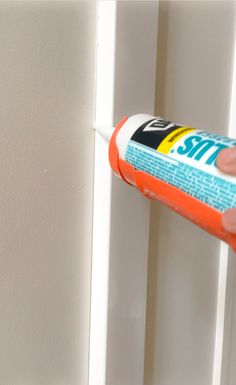 a hand holding a tube of glue on the side of a white painted door frame