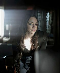 a woman with long hair sitting in a dark room looking at the camera and smiling