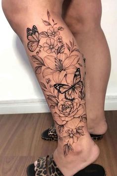 a woman's leg with flowers and butterflies on it, while she is wearing leopard shoes