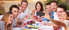 a group of people sitting around a table with wine glasses on it and one person taking a selfie