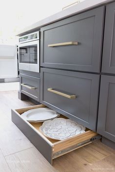 an open drawer in the middle of a kitchen with white plates and silver cupboards