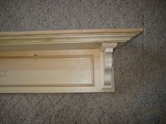 an unfinished wooden shelf on carpeted floor with white paint and wood trim around the edge