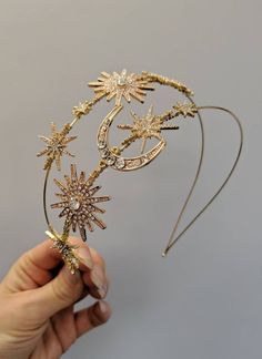 a person holding up a gold tiara with stars and moon decorations on it's head