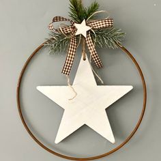 a white wooden star hanging on a circle with a ribbon and pine tree sprig