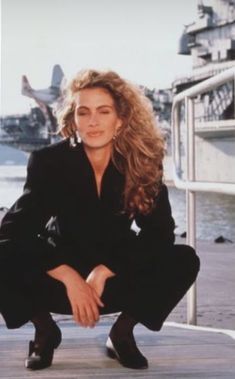 a woman is posing for a photo in front of the water and buildings with her hands on her knees