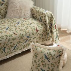 a living room with a couch and chair covered in a bird print fabric, next to a window