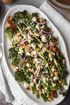 a white plate topped with broccoli covered in dressing next to a fork and knife