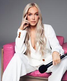 a woman sitting on top of a pink couch with a microphone in her hand and looking at the camera