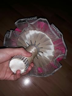 a hand holding a pink and white fan on top of a wooden floor