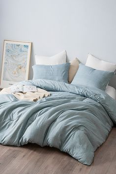 an unmade bed with blue comforter and pillows on the floor next to a painting