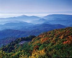 the mountains are covered in autumn foliage and trees with colorful leaves on them, as seen from an overlook point