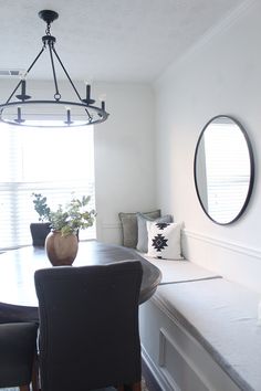 a dining room table with chairs and a bench in front of the window that has a round mirror hanging above it