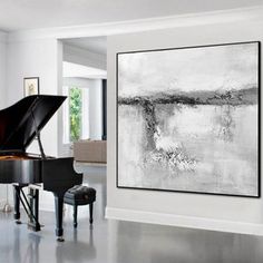 a large black and white painting hanging on the wall next to a piano in a living room