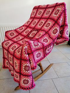 a pink crocheted blanket sitting on top of a wooden rocking chair