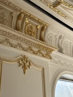 an ornate gold and white ceiling in a room with two windows, one has a clock on the wall