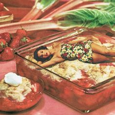 a woman laying on the ground next to some strawberries and other food in glass dishes