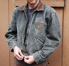 a man standing in front of a wooden door wearing a gray jacket and brown pants