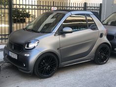 two smart cars parked next to each other in front of a fence and gated area