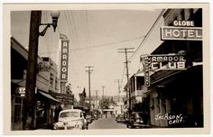 an old black and white photo of a street with cars parked on the side of it