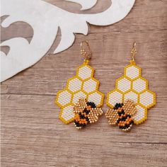 a pair of beaded bee earrings sitting on top of a wooden table