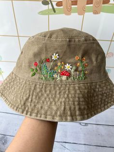 a woman's hat with flowers and mushrooms embroidered on the side, sitting in front of a tiled wall