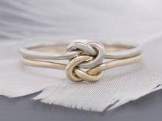 two tone gold and silver ring with an intertwined knot on the middle, sitting on top of a white feather