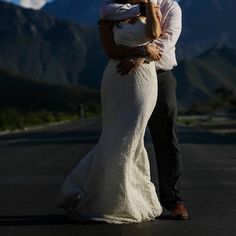 a bride and groom standing in the middle of an empty road with mountains in the background