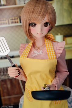 a doll holding a frying pan with a spatula in it's hand