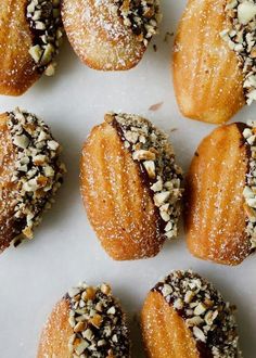 several pastries are lined up on a white surface with nuts and powdered sugar