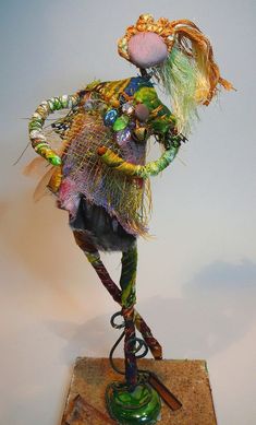 a sculpture of a woman with colorful hair and clothes on top of a wooden base