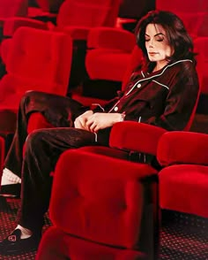 a woman sitting in a red chair with her hands on her knees and looking away from the camera