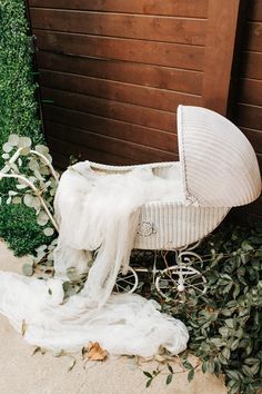 a white wicker baby's carriage sitting next to a wooden fence and shrubbery