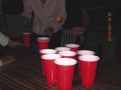 red plastic cups sitting on top of a wooden table next to people holding oranges