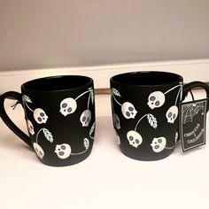 two black coffee mugs decorated with skulls and leaves