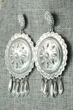 These sterling silver earrings were made by Navajo silversmith Terry Charlie. The back of the earrings are signed T. Charlie and stamped sterling.Length: 2 7/8"Width: 1 5/8"Free shipping on all orders! We ship with USPS and always include tracking. All orders ship within a day of payment.Returns are accepted up to 30 days after you receive your order. Just send us a message. Our shop offers cash back or store credit. The item must be returned in new condition. Southwestern Silver Concho Earrings, Elegant Silver Concho Earrings, Vintage Sterling Silver Etched Earrings, Vintage Etched Sterling Silver Earrings, Silver Concho Drop Earrings, Traditional Silver Concho Jewelry, Silver Dangle Earrings With Concho, Silver Concho Dangle Earrings, Native American Jewelry